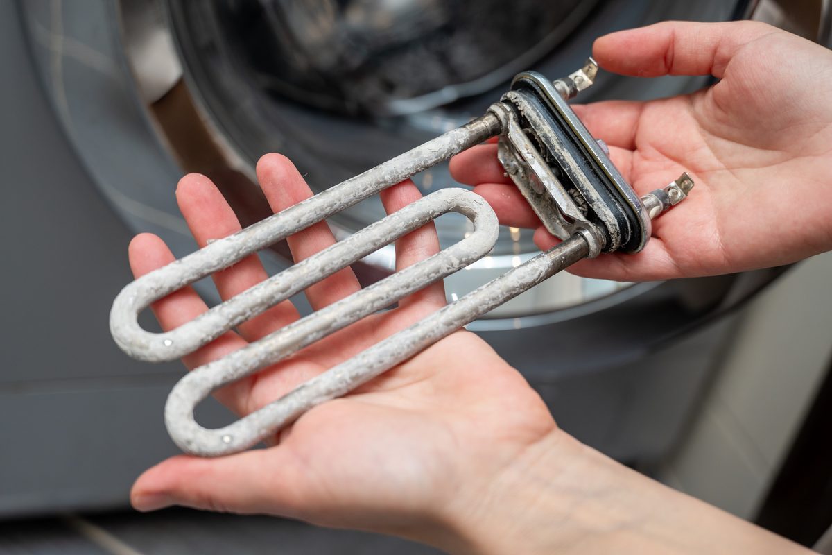 Hands holding a washing machine heating element thickly coated in hard scale